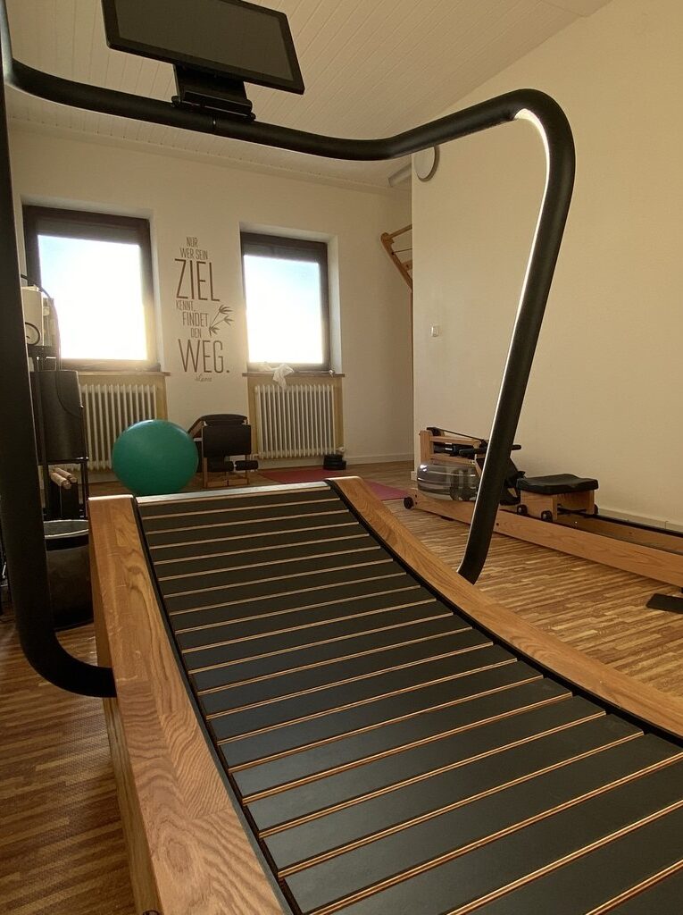 Curved Laufband in einem hellen Raum mit Fitnessgeräten und inspirierendem Poster an der Wand.