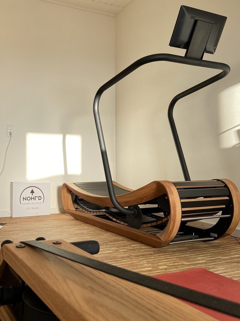 Modernes Rudergerät aus Holz mit geschwungener schwarzer Metallhalterung in einem hell erleuchteten Raum.