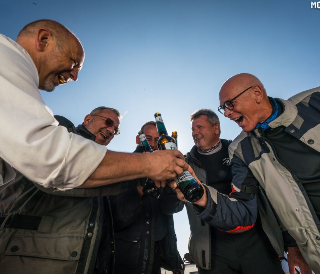 Fünf Männer stoßen im Freien bei Sonnenuntergang mit Bierflaschen an.