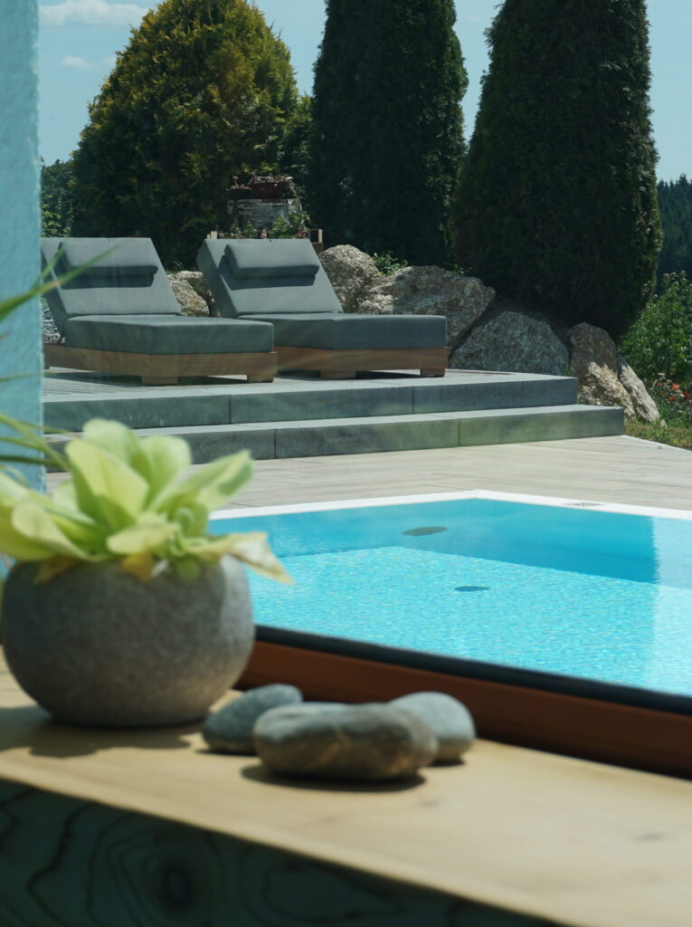 Luxuriöser Außenbereich mit einem Swimmingpool, stilvoll dekoriert mit einem Blumentopf und Steinen im Vordergrund, sowie modernen Liegestühlen im Hintergrund.