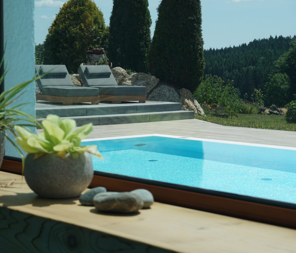 Außenpool mit Blick auf grüne Landschaft, umgeben von Liegestühlen und dekorativen Pflanzen.