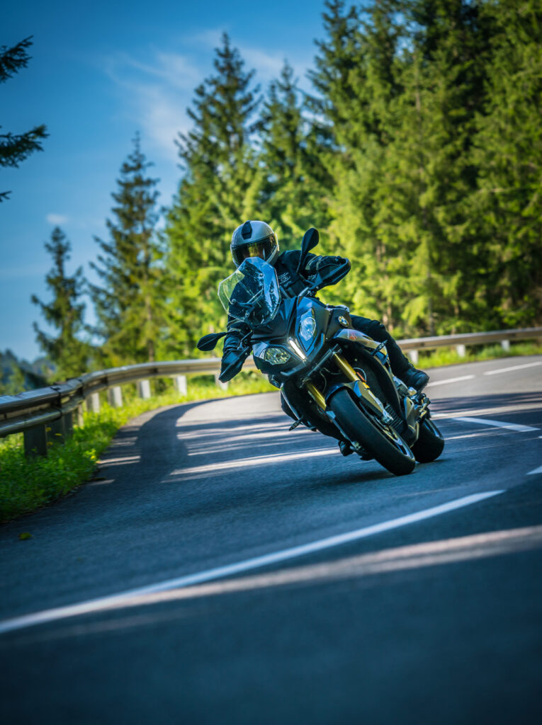 Motorradfahrer in voller Ausrüstung fährt eine Kurve auf einer waldreichen Landstraße.