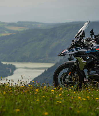 Motorrad der Marke BMW parkt auf einer Wiese mit Blick auf einen Fluss in einem Tal.