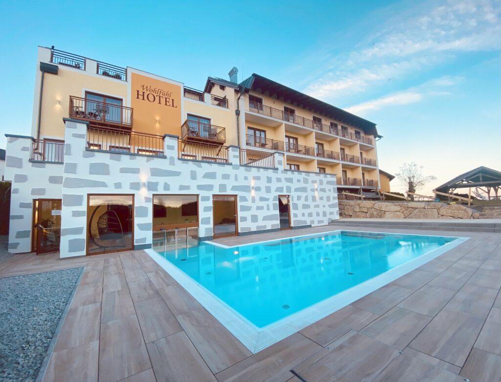 Ein großes Hotelgebäude mit mehreren Balkonen und einem Swimmingpool im Vordergrund unter klarem blauem Himmel.
