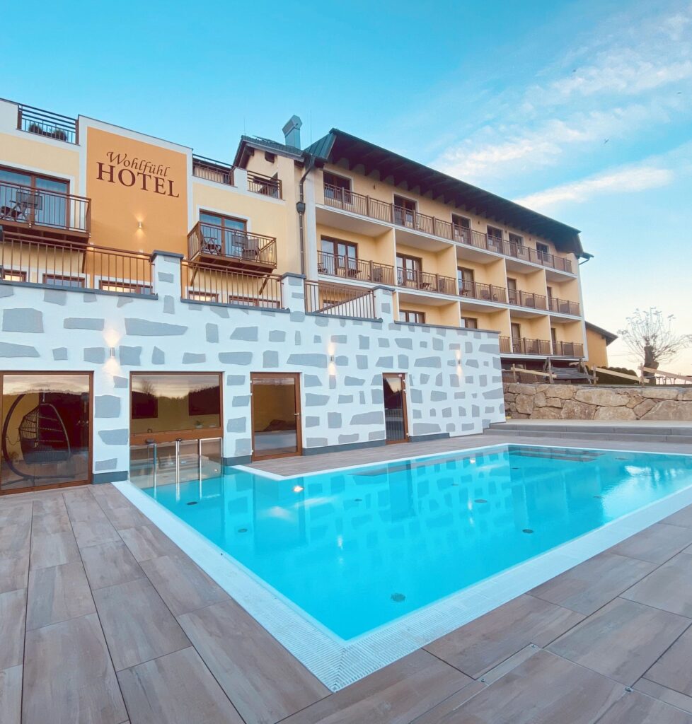 Außenansicht eines modernen Hotelgebäudes mit Schwimmbad bei Sonnenuntergang.