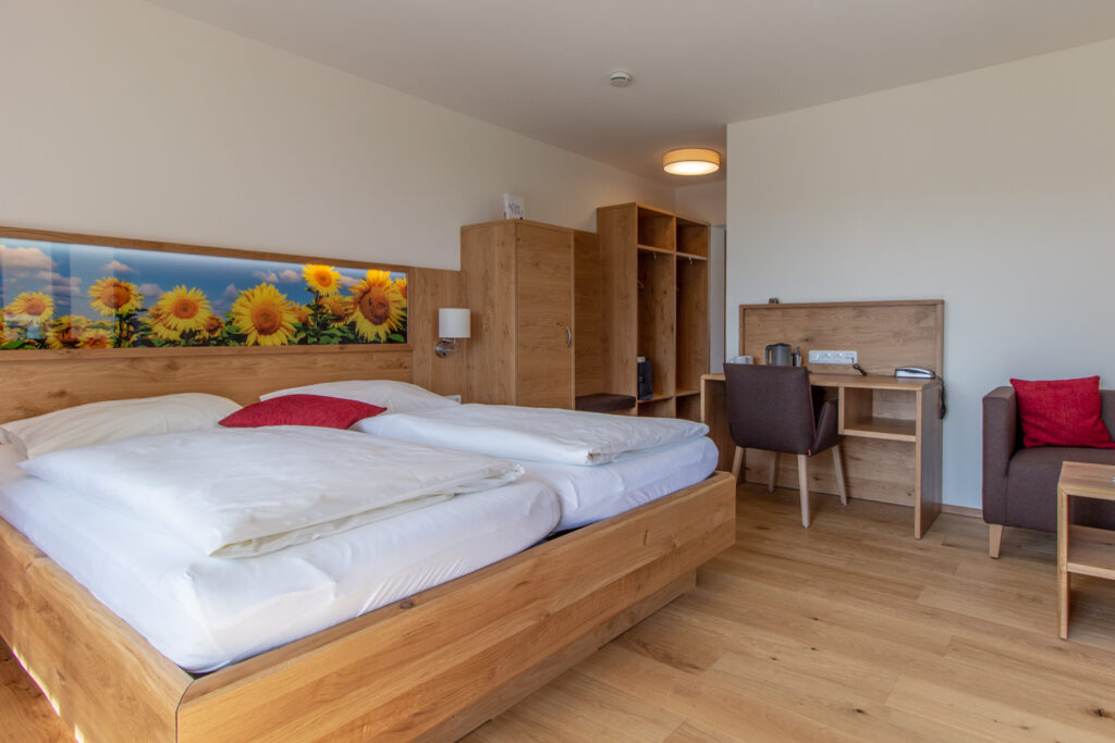 Helles Hotelzimmer mit einem Doppelbett, hölzernen Möbeln und einem großen Bild von Sonnenblumen über dem Bett.