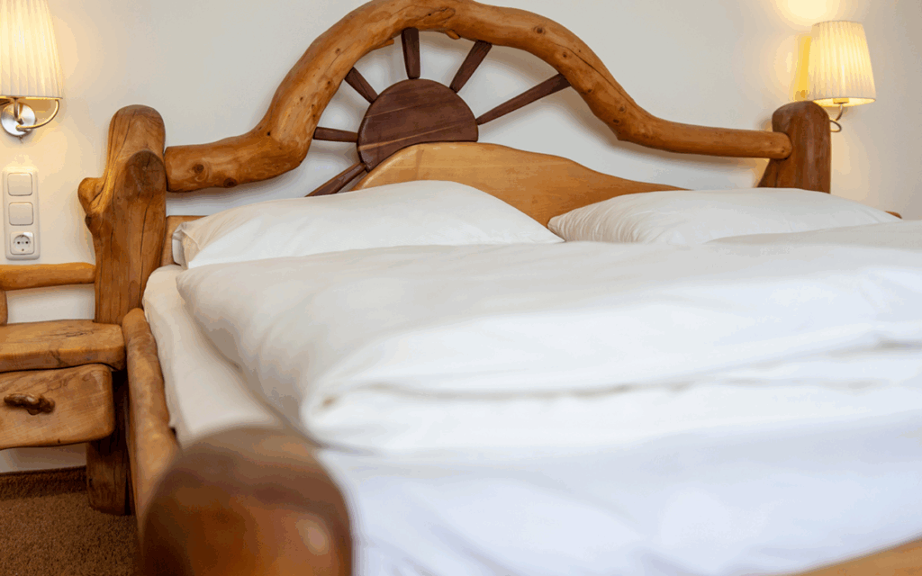 Rustikales Holzbett mit einem großen Kopfteil, das einem Steuerrad ähnelt, weißer Bettwäsche und eingeschalteten Nachttischlampen in einem gemütlich beleuchteten Schlafzimmer.
