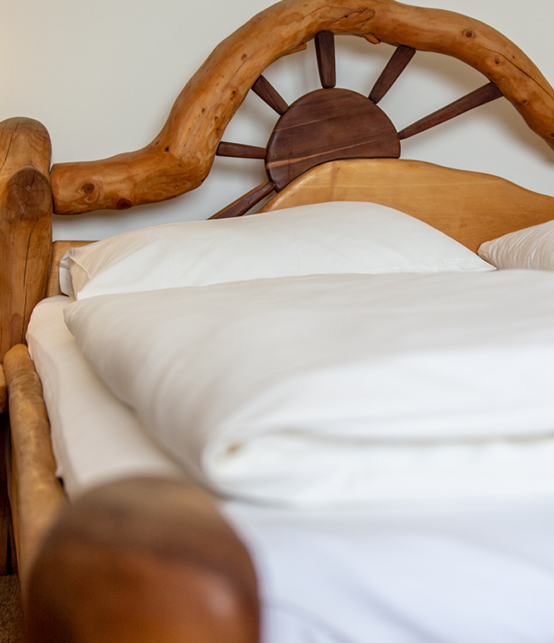 Bett mit einem Kopfteil aus einem Holzrad und organischen Formen, bezogen mit weißer Bettwäsche.
