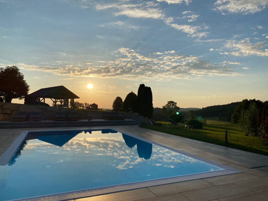 Sonnenuntergang über einem ruhigen Pool mit Blick auf eine hügelige Landschaft.