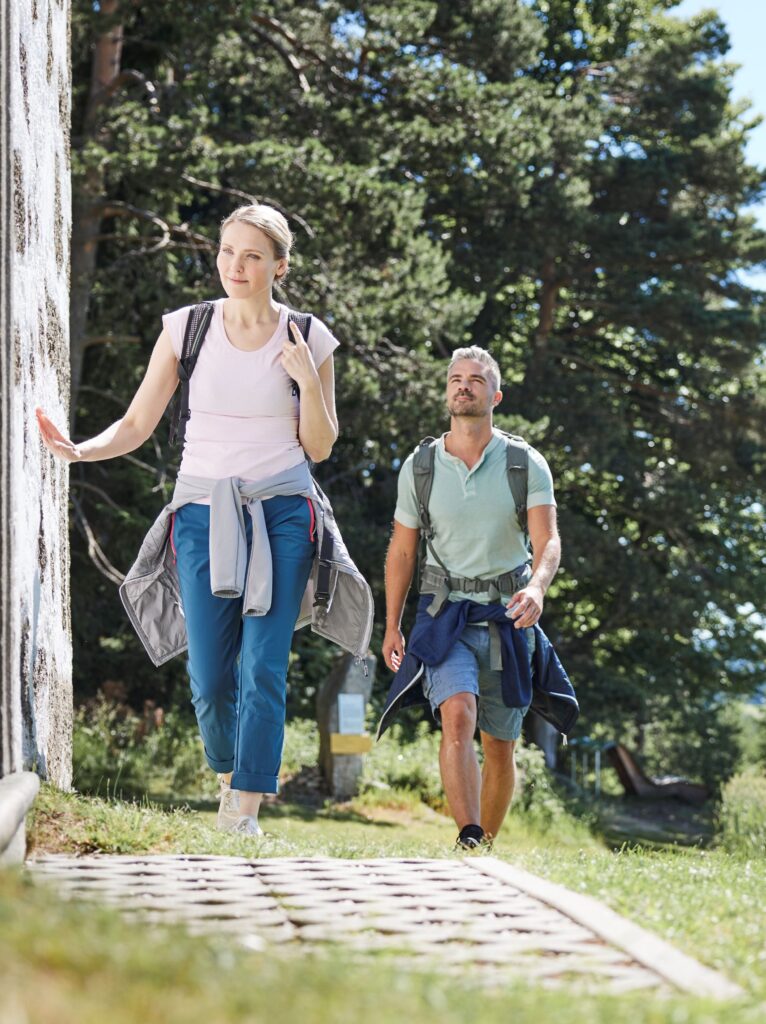 Zwei Personen beim Wandern in einem Wald auf einem Steinweg, eine Frau führt vor einem Mann.