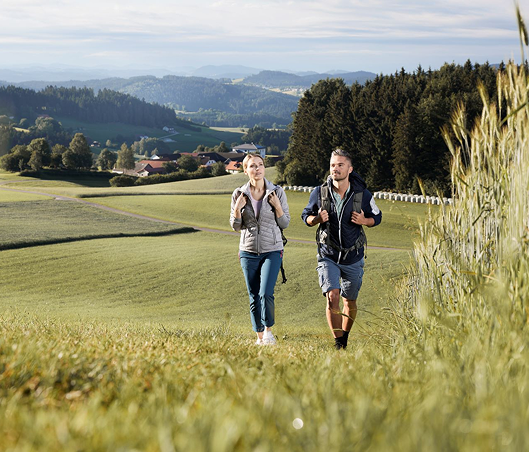 Junges Paar beim Joggen auf einem Feldweg in einer hügeligen Landschaft.