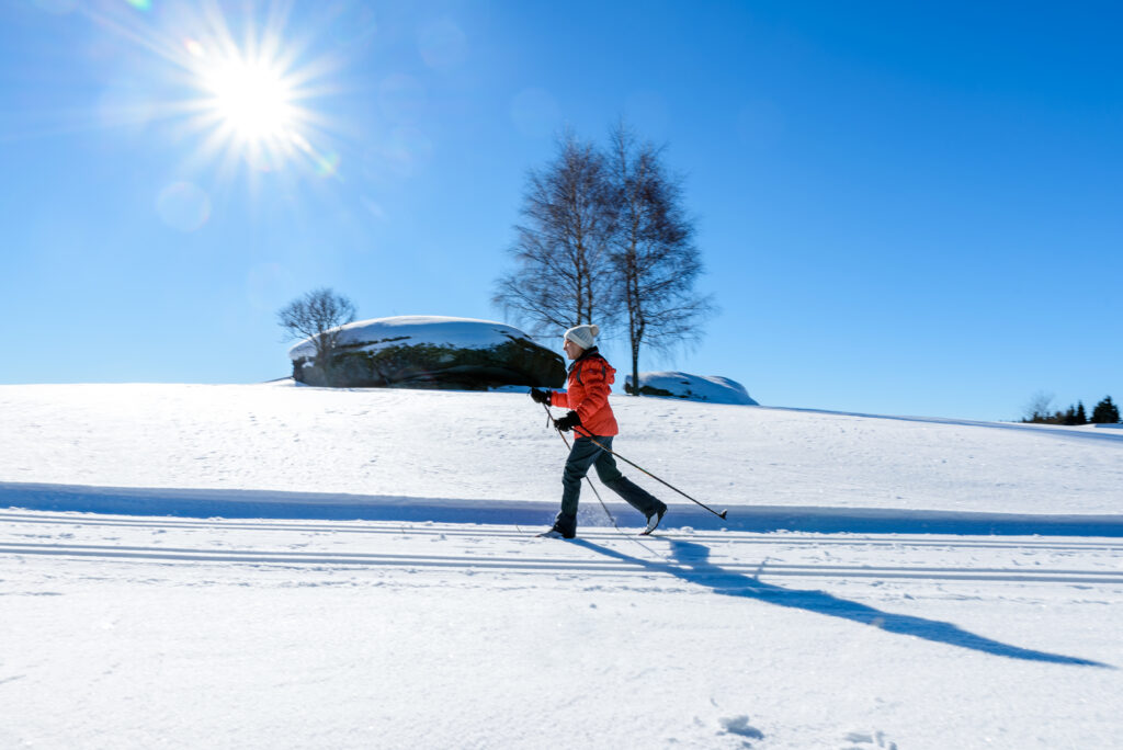 Person beim Langlaufen auf verschneiter Landschaft an einem sonnigen Tag.