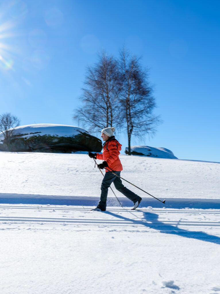 Eine Person in orangefarbener Jacke geht Langlaufen im Schnee unter blauem Himmel.