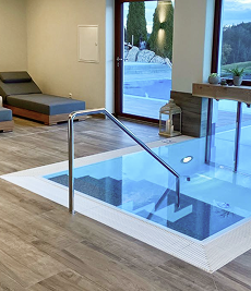 Modernes Innenpool mit Holzboden, klarem Wasser und großer Glastür, die zum Außenbereich führt.
