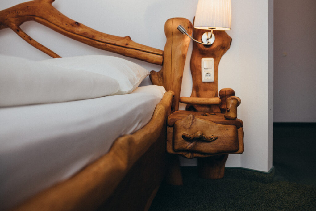 Gemütliches Schlafzimmer mit einem rustikalen Holzbett und Nachttisch, darauf eine eingeschaltete Tischlampe.
