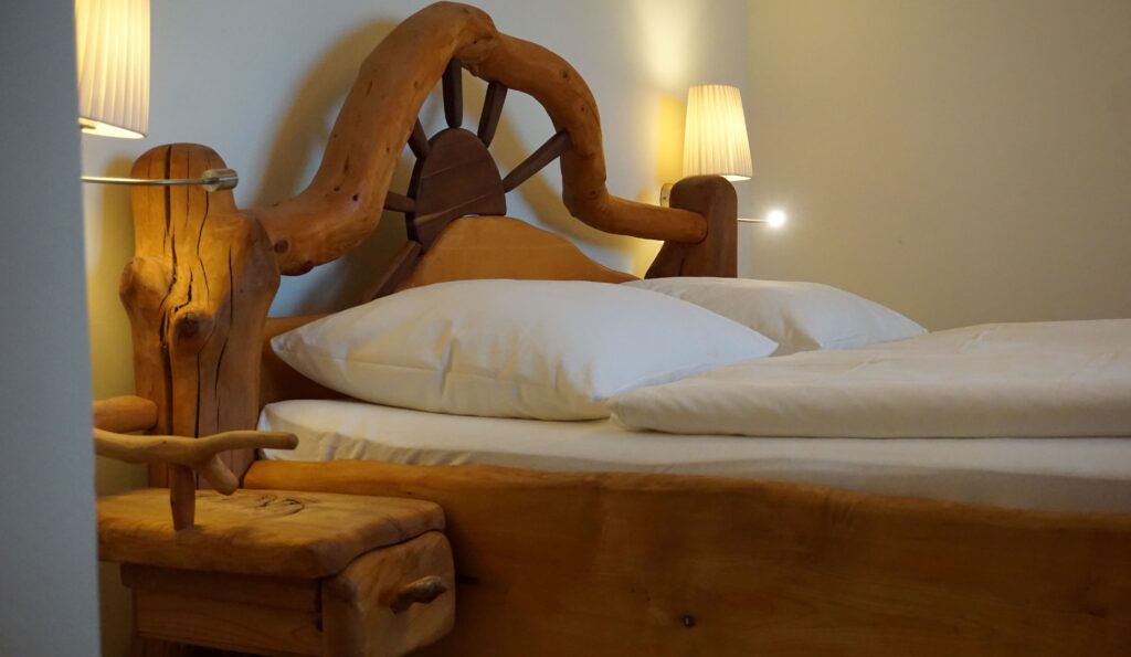 Ein gemütliches Schlafzimmer mit einem großen Bett, dessen Kopfteil aus natürlichem Holz gefertigt ist, flankiert von zwei Nachttischlampen.