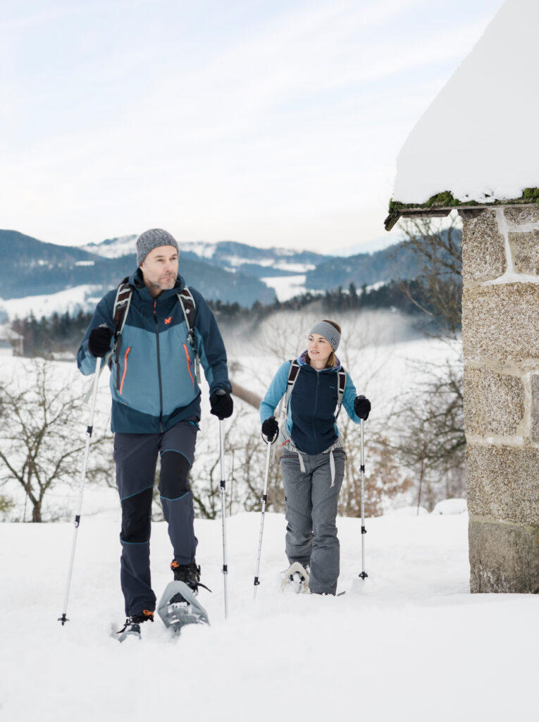 Ein Mann und eine Frau beim Schneewandern mit Stöcken in einer verschneiten Landschaft.