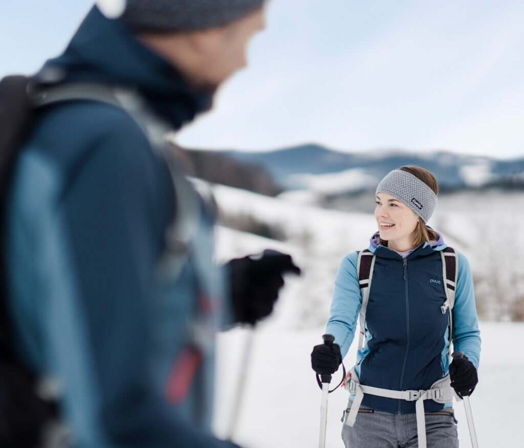 Zwei Personen beim Langlaufen im Schnee, eine Frau im Vordergrund lächelt einen Mann an.
