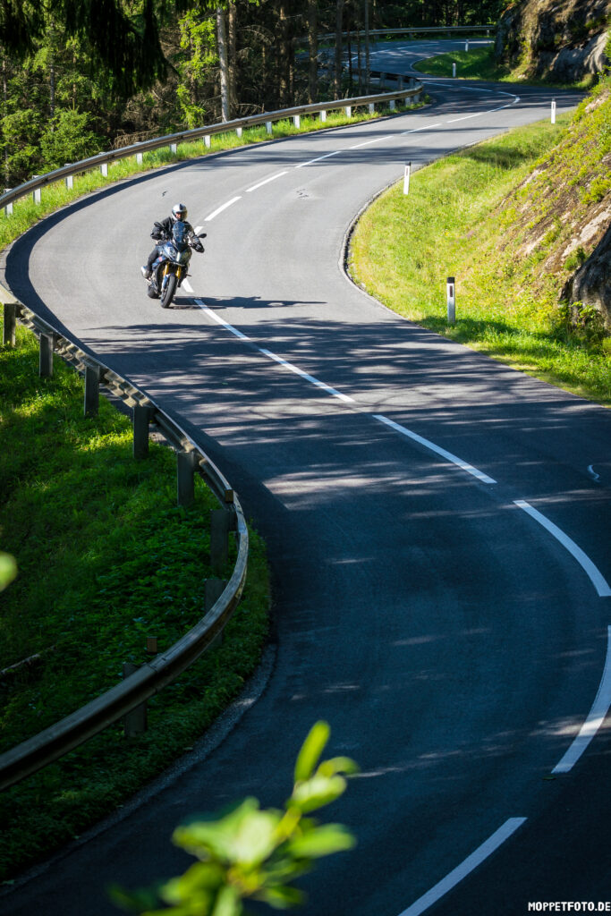 Motorradfahrer in einer scharfen Kurve auf einer bewaldeten Bergstraße.