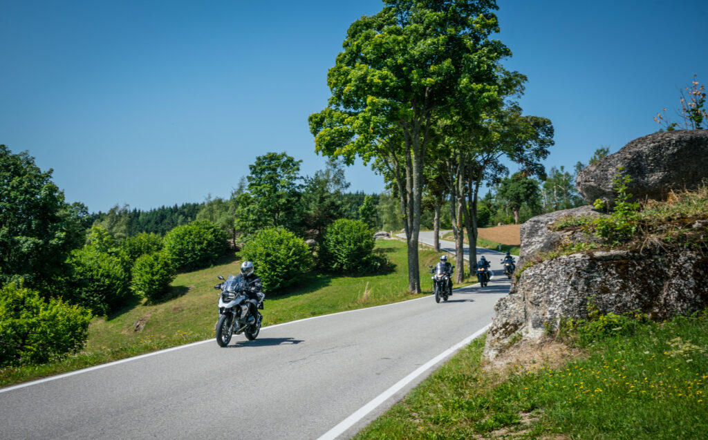Motorradfahrer auf einer kurvenreichen Landstraße bei sonnigem Wetter.
