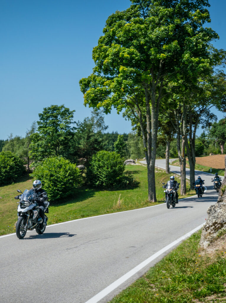 Motorradfahrer fahren auf einer kurvigen Landstraße bei sonnigem Wetter.