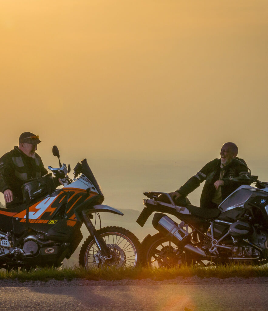 Zwei Motorradfahrer sitzen auf ihren Motorrädern und unterhalten sich bei Sonnenuntergang mit einem verschwommenen Hintergrund.