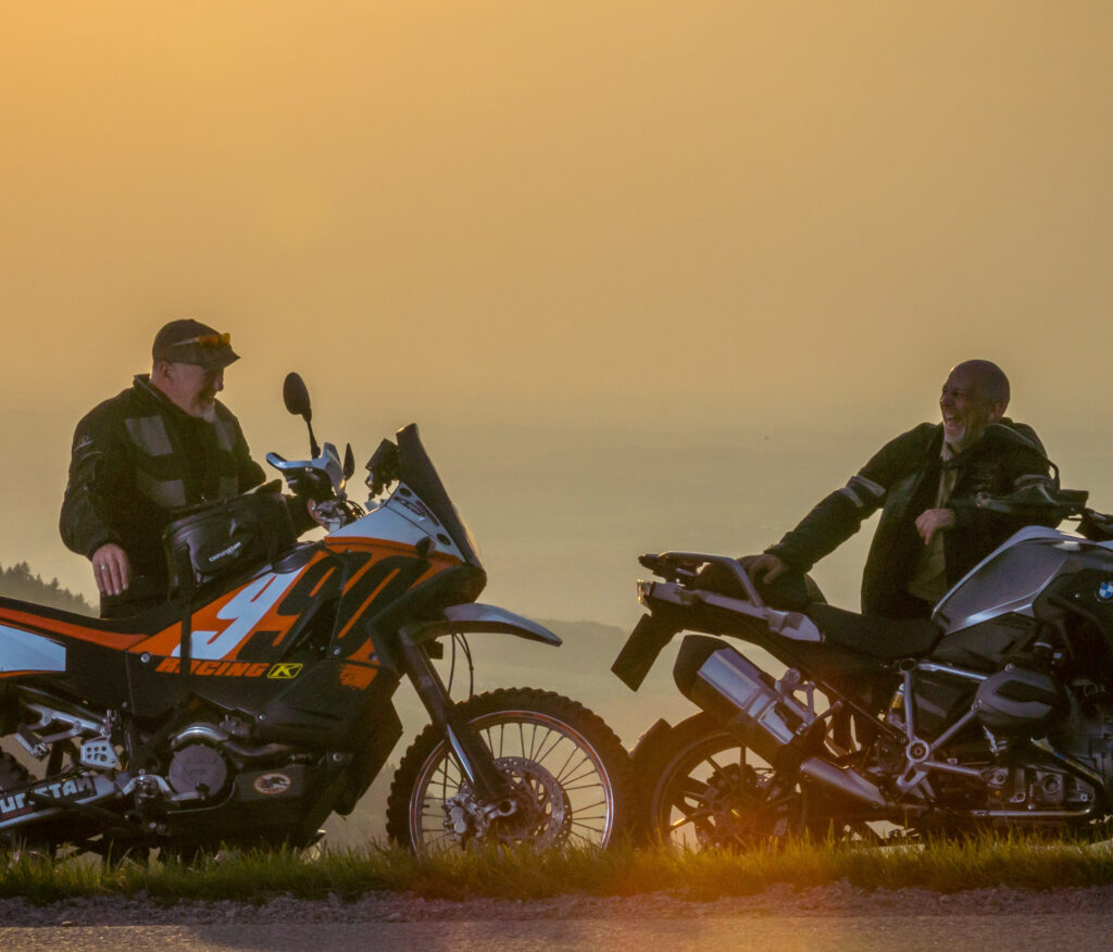 Zwei Personen sitzen auf Motorrädern und unterhalten sich bei Sonnenuntergang.