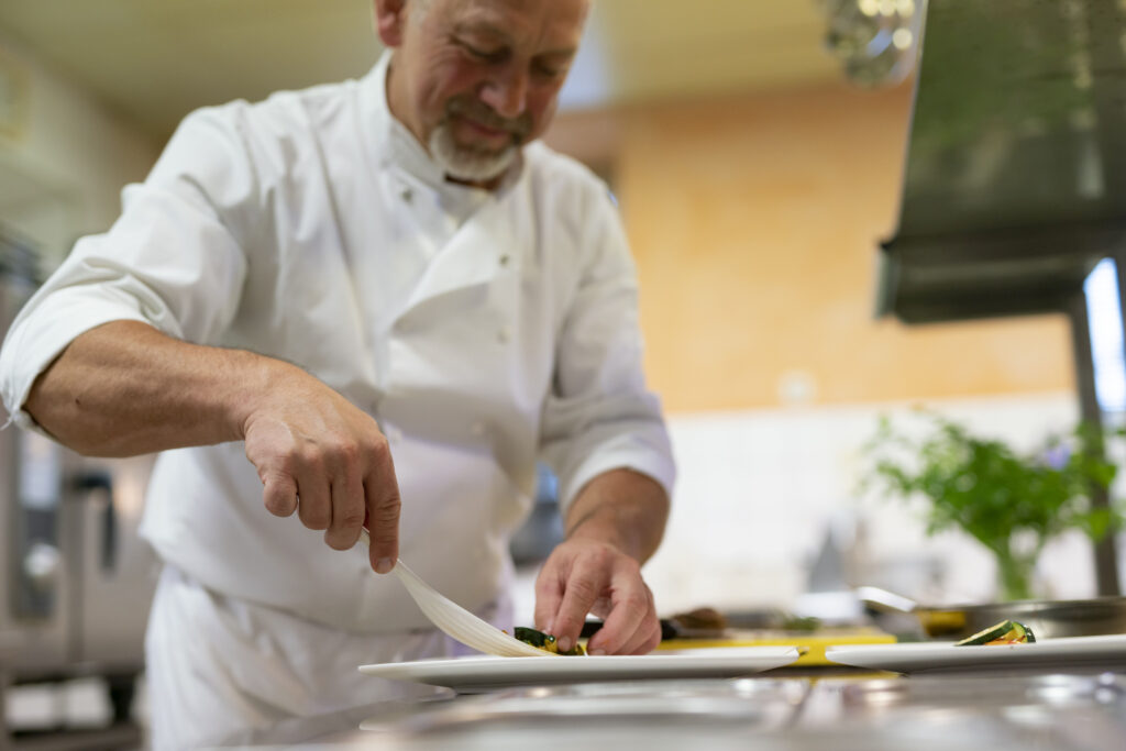 Ein erfahrener Koch garniert sorgfältig ein Gericht in einer Restaurantküche.