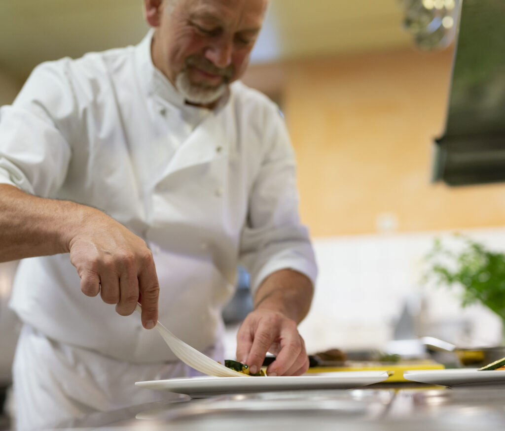 Älterer Küchenchef garniert sorgfältig ein Gericht in einer professionellen Küche.