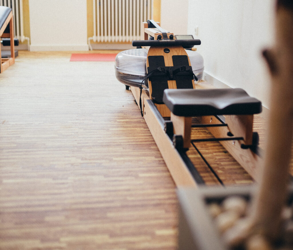 Ein Rudergerät aus Holz in einem hellen Fitnessraum mit Parkettboden.