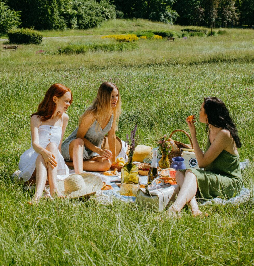 Drei Frauen sitzen bei sonnigem Wetter auf einer Wiese und genießen ein Picknick.